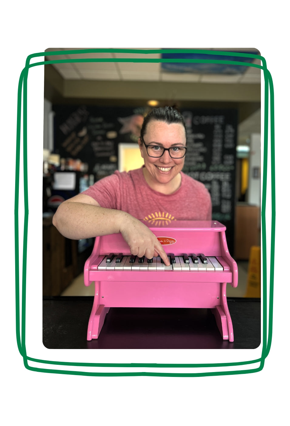 Jenn, the owner of the Pink Piano Cafe & Lounge, smiling and pressing a key on a small pink piano. 